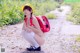 A woman in a yellow hat and white tights crouching down on a dirt road.