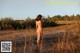 A naked woman standing in a field of tall grass.