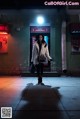 A woman walking down a sidewalk in front of a neon sign.