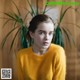 A woman in a yellow sweater sitting in front of a plant.