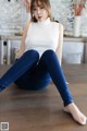 a woman sitting on the floor wearing a white top and blue jeans