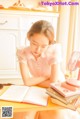 A young girl sitting at a table with a fan and books.