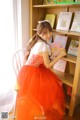 A woman in a red dress sitting on a chair in front of a book shelf.