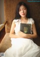 A woman in a white dress sitting on a chair holding a book.