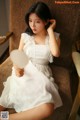 A woman in a white dress sitting on a chair holding a mirror.