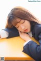 A woman in a school uniform sleeping on a desk.