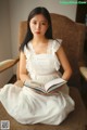 A woman in a white dress sitting in a chair reading a book.