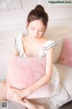 A woman sitting on a couch holding a pink pillow.