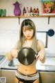 A woman in lingerie holding a frying pan in a kitchen.