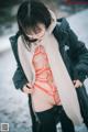 A woman in a black jacket and orange bikini standing in the snow.