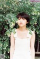 A woman in a white dress standing in front of a bush.