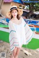 A woman in a white dress and straw hat standing next to a boat.