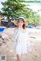 A woman in a white dress and hat on a beach.