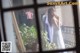 A woman in a white dress standing in front of a window.