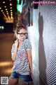 A woman wearing glasses leaning against a wall.