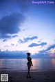 A woman in a bikini standing on a beach at sunset.