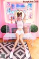 A woman sitting on a white bench in front of a pink wall.