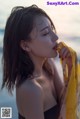 A woman in a black bathing suit holding a yellow scarf.