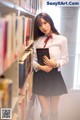 A woman standing in front of a bookshelf holding a book.