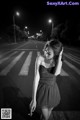 A woman in a black dress standing on the side of a road.