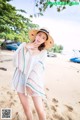 A woman in a white dress and straw hat on a beach.