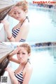 A woman in a striped bathing suit leaning against a wall by a pool.