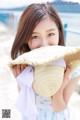 A young woman holding a straw hat on the beach.