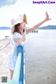 A woman in a blue dress and a straw hat standing on a pier.