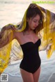 A woman in a black bathing suit standing on the beach.