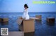 A woman in a white dress sitting in a cardboard box in the water.