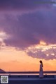 A woman in a long dress standing on a pier at sunset.