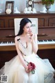 A woman in a wedding dress sitting in front of a piano.