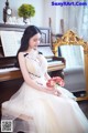 A woman in a wedding dress sitting on a piano.