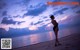 A woman in a bikini standing on a beach at sunset.