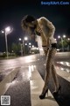 A woman in fishnet stockings and high heels standing in the rain.