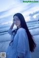 A woman with long black hair standing on a beach.