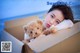 A woman laying in a cardboard box holding a teddy bear.