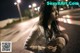 A woman sitting on the side of a road at night.