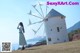 A woman standing in front of a windmill on a hill.