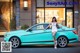 A woman leaning on the hood of a blue car.