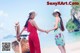 Two women holding hands on a beach next to a boat.