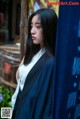 A woman with long black hair standing in front of a blue curtain.