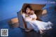 A woman in a white dress sitting in a cardboard box holding a teddy bear.