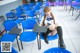 A woman sitting on a blue chair in a classroom.