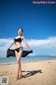 A woman in a black bikini standing on a beach.