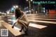 A woman sitting on the crosswalk in the middle of the street.