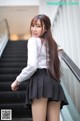 A woman in a white shirt and black skirt posing on an escalator.