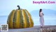 A woman standing next to a large yellow pumpkin.