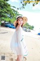 A woman in a white dress and hat standing on a beach.