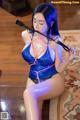 A woman in a blue latex outfit holding a whip.